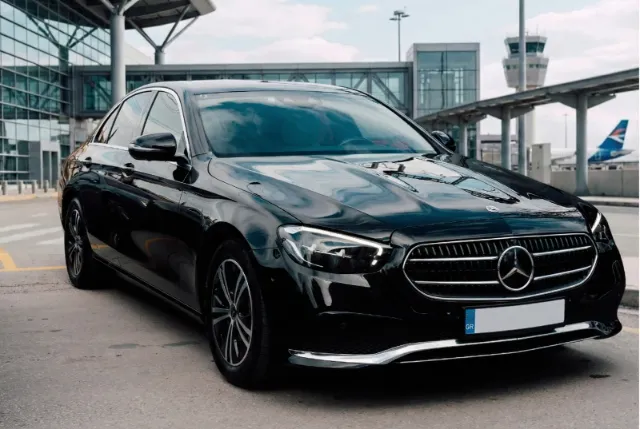 Black Mercedes-Benz E-Class sedan of Unique Transfers & Tours outside an airport terminal