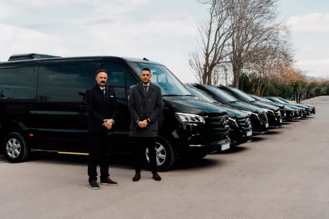 Two Unique Transfers & Tours chauffeurs standing beside a black Mercedes-Benz minibus
