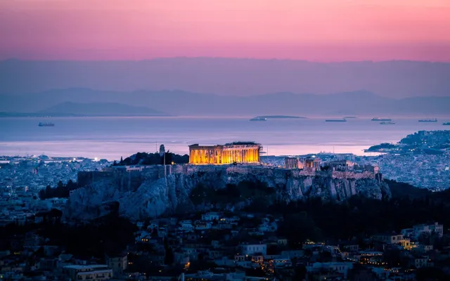 The floodlit Acropolis at dusk with the Saronic Gulf and ships on the horizon