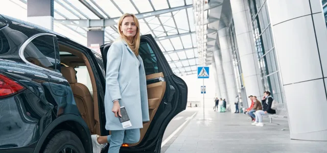 Traveller stepping out of a dark car at an airport departures kerb