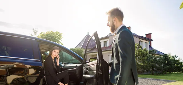 Chauffeur in a dark suit opening the rear door of a car for a passenger