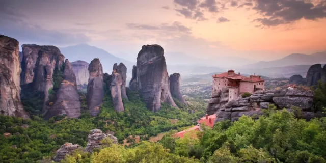 A Meteora monastery on a ledge below the tall rock pillars at sunset